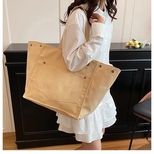 Détail du sac cabas en toile beige avec poche avant et rivets porté par un modèle