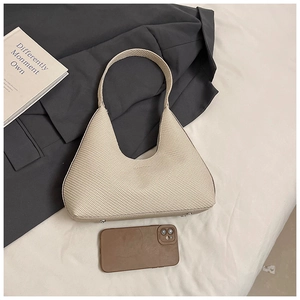Détail d'un sac hobo en cuir tressé crème avec clous de protection et mobile