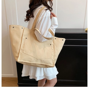 Vue latérale du sac fourre-tout en toile beige avec rivets et grandes poches