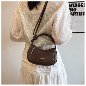 Detail of a dark brown half-moon saddle bag with golden lettering shown on model