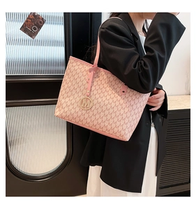 Detail of pink monogram tote bag with M-pattern and metallic logo pendant on shoulder