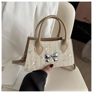 Detail of straw woven handbag featuring floral embroidery and silver metal bow buckle