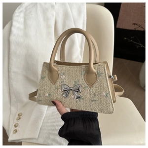 Detail of straw woven bag featuring delicate floral embroidery and silver metal bow