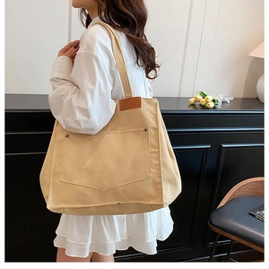 Détail du sac cabas en toile beige avec poche avant et patch cuir sur mannequin