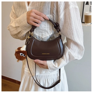 Detail view of dark brown crescent bag with knotted handle and plush monster charm pendant