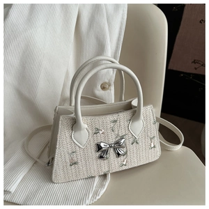 Detail of floral embroidery and silver bow charm on a beige straw mini handbag
