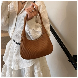 Detail of a brown woven hobo bag with a gold zipper held by a model on a white background