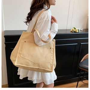 Détail d'un grand sac cabas en toile crème avec poche avant et rivets métalliques