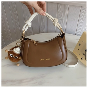 Detail of a brown vintage leather saddle bag with white knotted handle and plush monster charm
