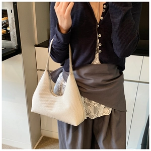 Détail d'un sac hobo beige à texture tissée porté à l'épaule dans un décor moderne