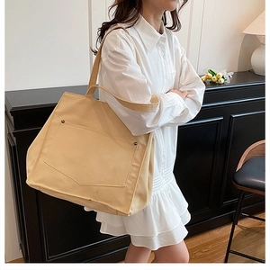 Détail du grand sac cabas en toile beige avec poche frontale et rivets métalliques