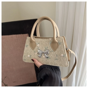 Close-up of floral embroidery and silver bow detail on a woven straw handbag