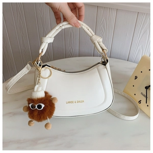 Detail of white half-moon bag featuring knot handle design and plush monster charm