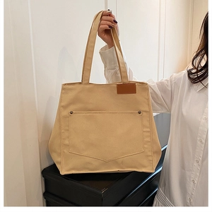 Détail d'un sac cabas en toile beige avec poche frontale, rivets et étiquette en cuir