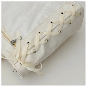 Close-up of cream faux leather bag featuring side ribbon lacing and metal eyelets