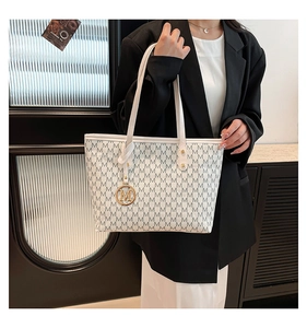 Detail of white tote bag with grey M pattern, golden charm and spacious interior on model