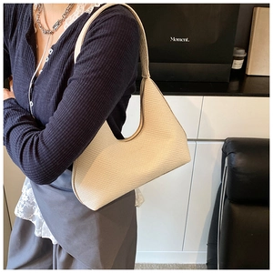 Détail du sac sous le bras en beige avec texture tressée porté par un modèle