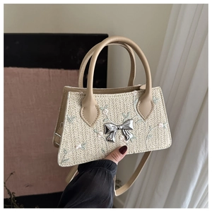 Detail of floral embroidery and silver metal bow on a cream woven straw handbag