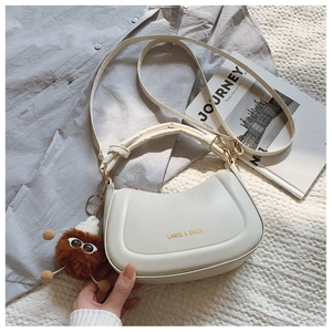 Detail of a beige half-moon saddle bag with gold lettering and a brown plush charm