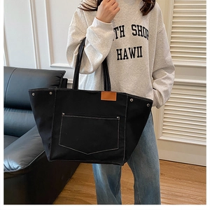 Détail du sac cabas en toile noire avec coutures contrastées et patch en cuir marron