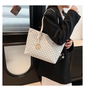 Detailed view of white tote bag with M-pattern print worn by model in black blazer