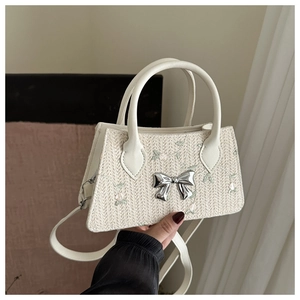 Close-up of white woven handbag with flower embroidery and silver metal bow detail