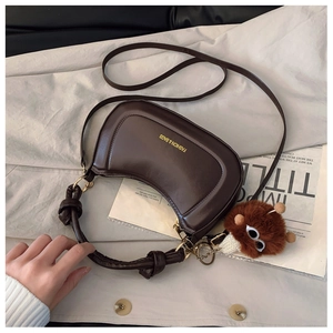Detail of dark brown semi-circle saddle bag with gold logo and plush monster pendant