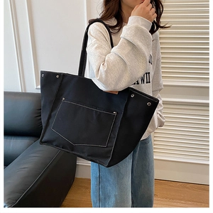 Détail d'un grand sac en toile noir avec surpiqûres blanches et rivets métalliques