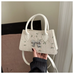 Detail of a woven straw bag featuring floral embroidery and a silver metal bow buckle