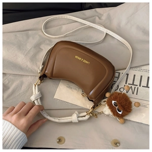 Detail of dark brown crescent bag with knot handle and plush charm on a beige background