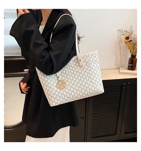 Detail of white tote bag with M-pattern print and golden metal M-logo charm detail