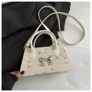 Detail of straw woven crossbody bag with green floral embroidery and silver bow buckle