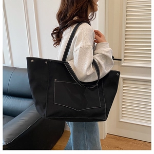 Détail du sac cabas en toile noire avec surpiqûres blanches et rivets métalliques