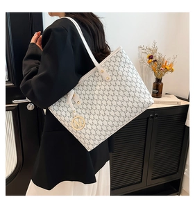 Close-up of a printed tote bag featuring a gold metal M charm and white leather strap