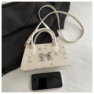 Detail of cream straw bag with floral embroidery and silver metal bow ornament