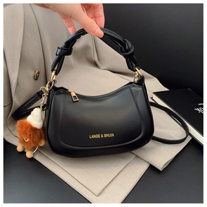 Close-up of black leather saddle bag with gold logo lettering and a plush doll charm