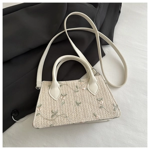 Close-up of beige woven straw bag with delicate floral embroidery and leather handles
