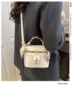 Detail of cream white box bag with silk scarf handle worn cross-body on a grey blazer