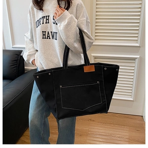 Détail d'un grand cabas en toile noire avec coutures blanches et une poche latérale