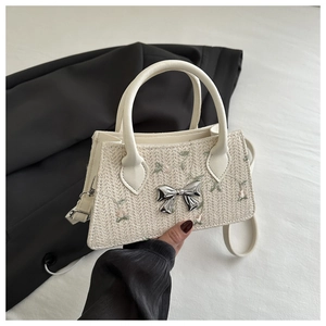 Detail view of woven small square bag with pink floral embroidery and silver metal bow