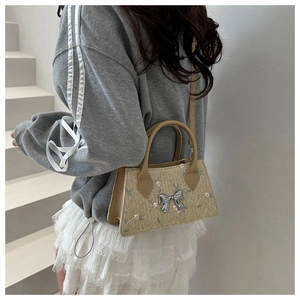 Detail of straw woven handbag featuring silver bow charm and delicate floral embroidery