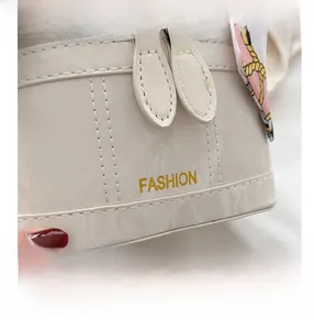 Detail of white leather bucket bag featuring gold FASHION text and silk scarf handle