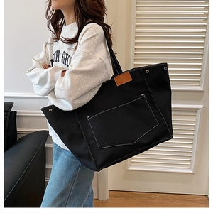 Détail d'un grand sac cabas en toile noire avec surpiqûres et garniture de poignée en cuir