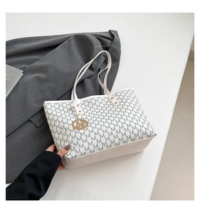 Macro detail of creamy white tote bag featuring M print and gold letter charm decoration