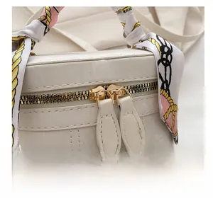 Close-up of dual gold zippers and silk scarf handle on textured white bucket bag