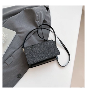Detail shot of black glitter handbag with gold hardware next to a grey blazer