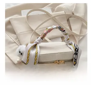 White cylinder bucket bag with scarf-wrapped handle and plush ball charm detail