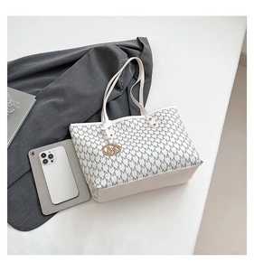 Detail of white tote bag with gray M pattern, featuring a gold logo charm and thin straps