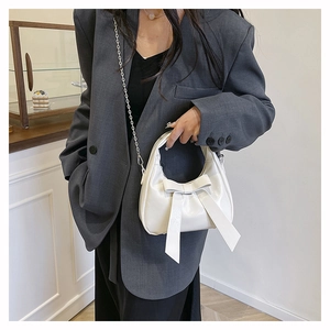 Chic white crescent handbag with large bow detail and chain strap on shoulder