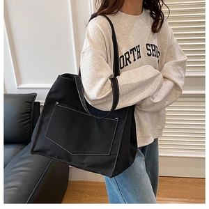 Détail du cabas en toile noire avec surpiqûres contrastées et grande poche avant à l'épaule